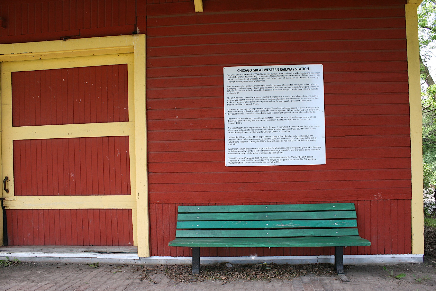 Green bench under the Chicago Great Western Railway Station history plaque beside the freight door