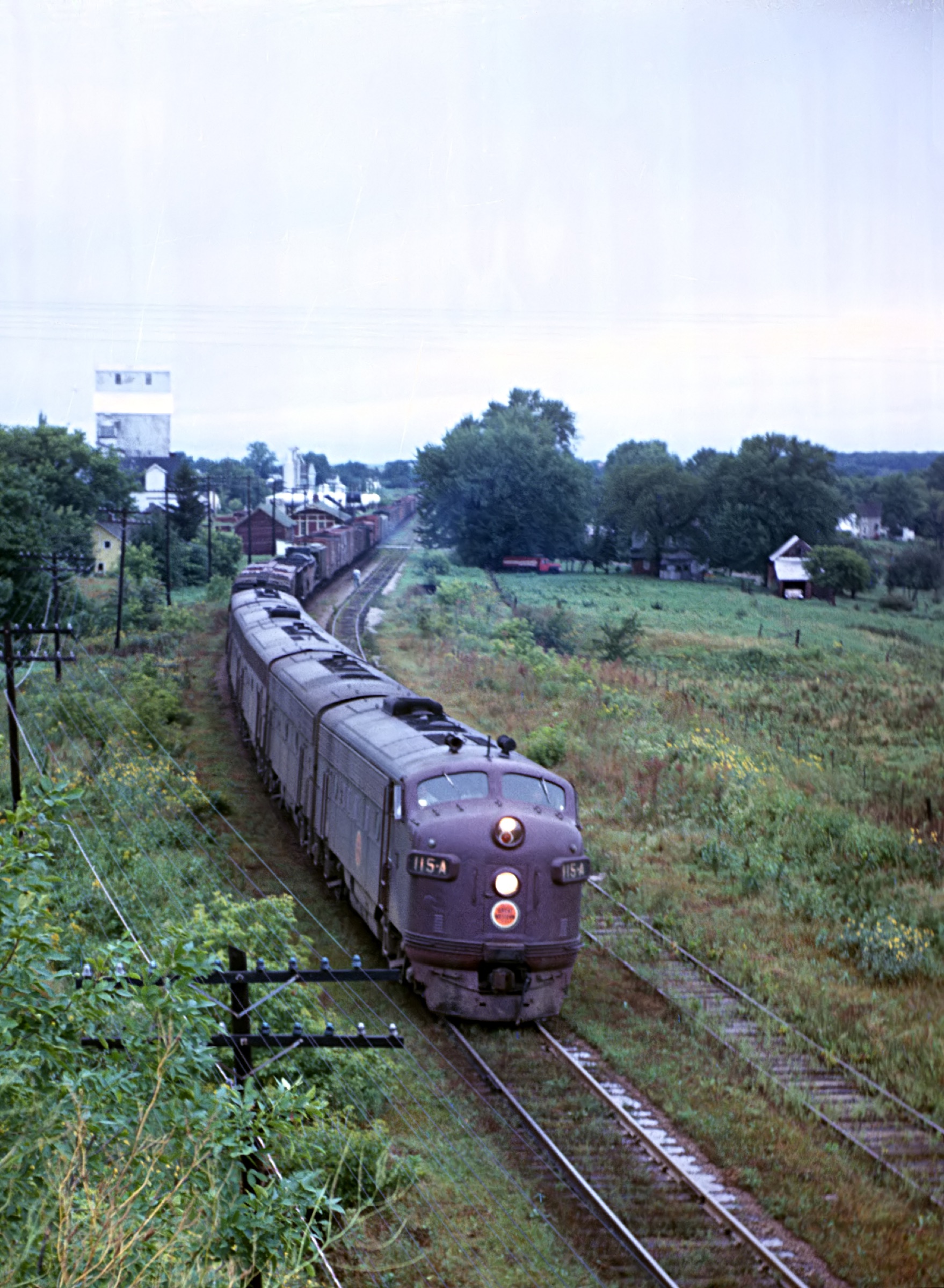Chicago Great Western locomotive 115-A leading Train 43 through Kenyon, Minnesota, August 31, 1962, with the grain elevator behind